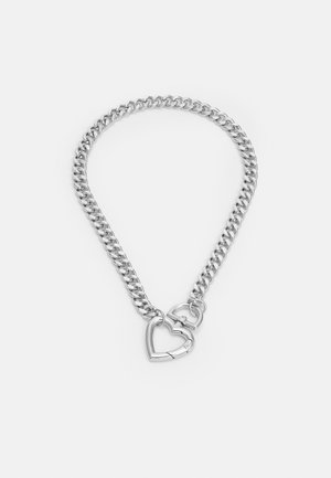 Zilveren ketting met dikke schakels en twee hartvormige sluitingen die de uiteinden verbinden op een witte achtergrond.