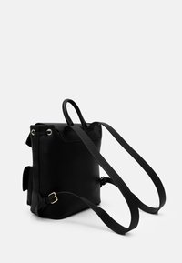 Svart strukturerad läderryggsäck med justerbara remmar, handtag på toppen och metallhardware-accenter, med rektangulär form och minimalistisk design.