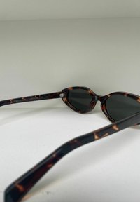  schildpadbril met cat-eye vorm, donkere lenzen en slanke, gebogen armen. Voorzien van merking op de binnenkant van de arm.