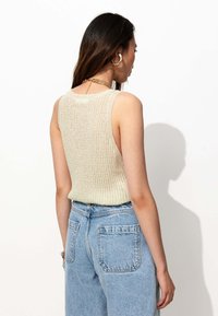 Débardeur en tricot beige avec un design texturé et de larges emmanchures, associé à un jean taille haute bleu clair avec des poches arrière.