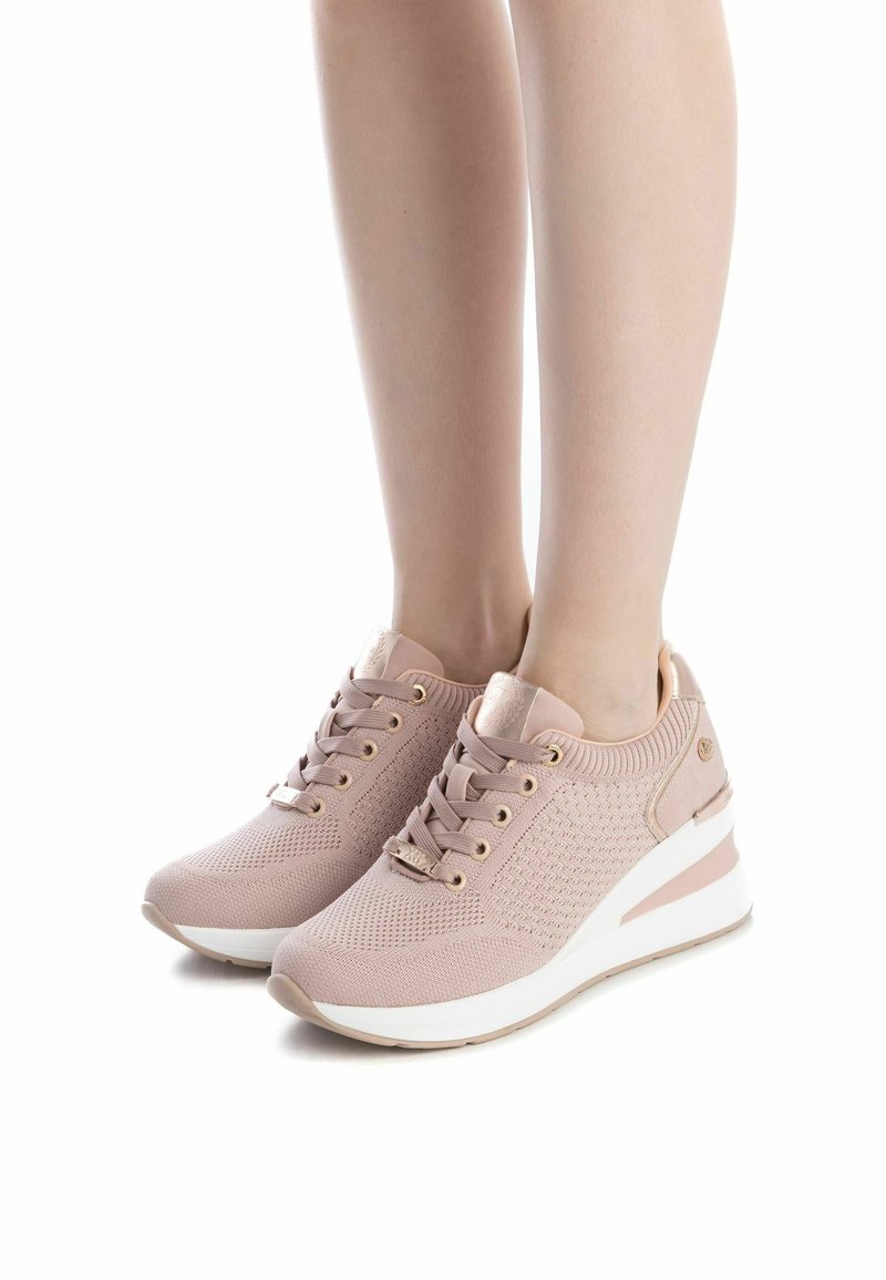 Zapatillas de punto de color rosa claro con un acabado texturizado, cuentan con una entresuela blanca, detalles en dorado y cordones planos. Puntera redondeada, diseño de perfil bajo.