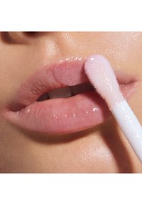 Clear läppglans applicerat med en applikator med rosa topp på släta, lätt glansiga, ljusrosa läppar. Huden verkar mjuk och något upplyst.