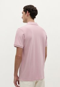 Polo shirt rose à manches courtes avec col, fabriqué dans un tissu respirant et texturé. Les fentes sur les côtés assurent une liberté de mouvement.