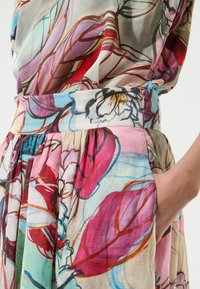 Robe à imprimé floral présentant un motif multicolore avec des nuances de rose, bleu et rouge. Conçue en tissu léger avec un design plissé.