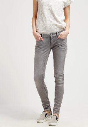 Grijze skinny jeans met een vervaagde textuur, vijf pockets en metalen knoopsluiting, gecombineerd met een licht gestreept T-shirt met korte mouwen.