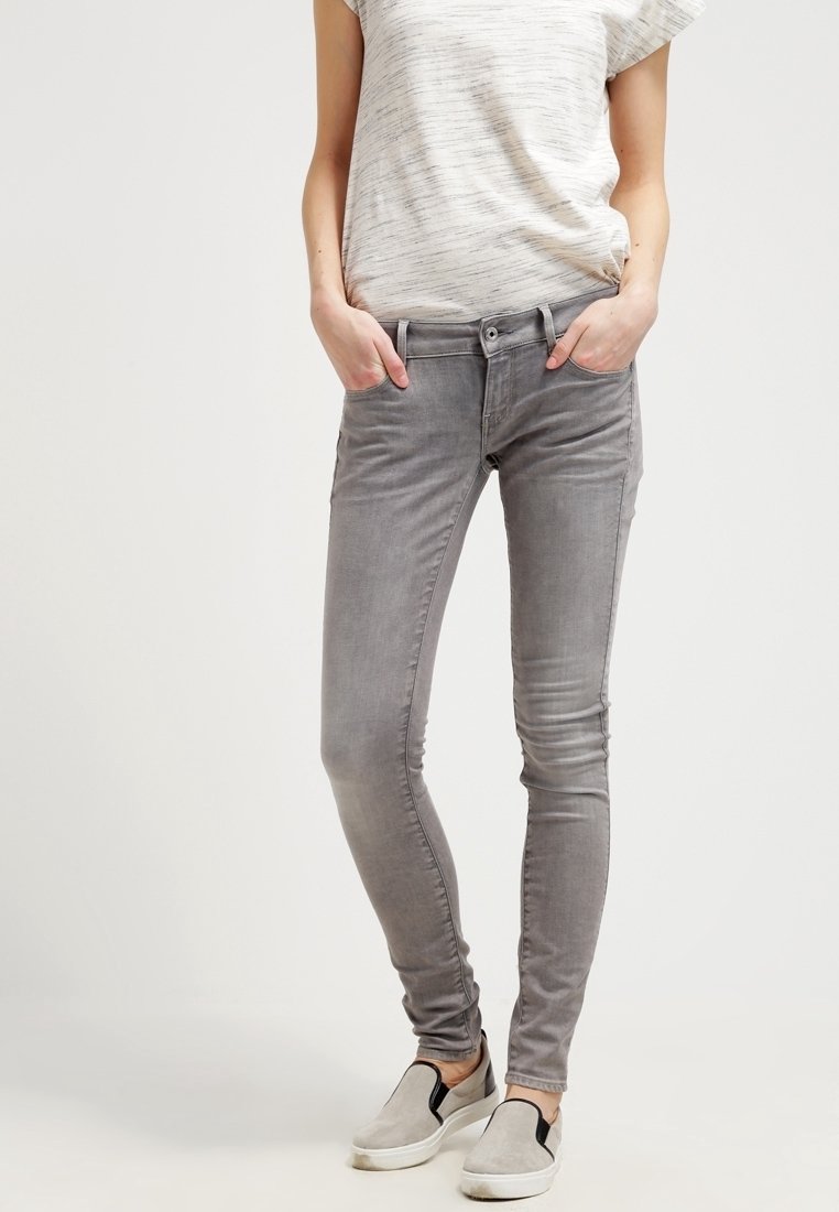 Jeans ajustados grises con una textura deslavada, diseño de cinco bolsillos y cierre de botón metálico, combinados con una camiseta de rayas de manga corta ligera.