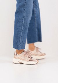 Chaussures de sport beiges et métalliques avec des accents réfléchissants et des languettes rembourrées, assorties à un jean denim bleu coupé court.