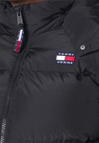 Giacca imbottita nera con zip frontale, caratterizzata da un piccolo logo ricamato di Tommy Jeans in rosso, bianco e blu sul petto.
