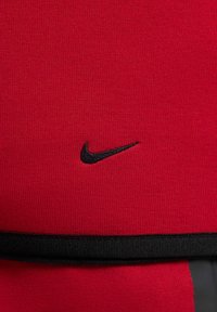 Camisa atlética roja hecha de una tela texturizada, con el logo de Nike en negro y una banda de acento negra en la parte inferior.