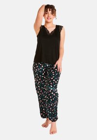 Débardeur noir avec bord en dentelle, associé à un pantalon de pyjama noir orné d'un motif floral rose et vert sur un fond sombre.
