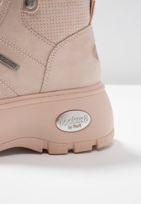 Ljust rosa mockastövel med perforerad textur, silvriga hårdvarudetaljer med logotyp och en tjock gummisula med greppaccenter.