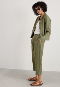 Chaqueta de lino verde oliva con pantalones de tiro alto a juego, combinada con una blusa blanca y sandalias de piel marrón con tiras.