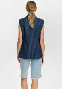 Tume sinine ilma varrukateta bleiser, millel on triibuline muster, kohandatud disain ja struktureeritud õlad; kombineeritud kergelt kulunud teksashortsidega.