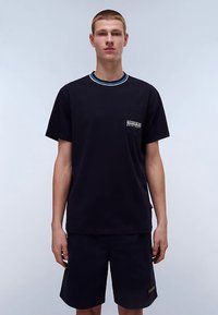 Czarny bawełniany t-shirt z okrągłym dekoltem, kontrastowymi paskami i małą kieszonką na piersi z logo. Noszony z pasującymi czarnymi szortami.