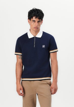 Navy knitted polo shirt with a white collar and half-zip, featuring striped accents in beige and black, and a small logo on the chest.