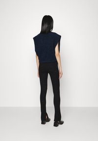 Marineblauwe gebreide top met brede armgaten, gecombineerd met zwarte legging met zilveren spikkels en zijsplitten, gedragen met stevige zwarte schoenen.