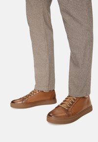 Zapatillas de cuero marrón con una textura suave, que presentan seis ojales, cordones en contraste y una suela de goma, combinadas con pantalones de cuadros.