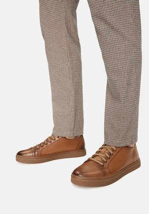 Hnedé kožené tenisky s hladkou textúrou, obsahujúce šesť dierok, kontrastné šnúrky a gumovú podrážku, kombinované s kockovanými nohavicami.