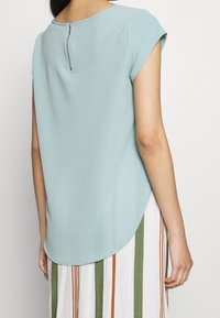 Ljusblå kortärmad topp i texturerat tyg med rundad nederkant och dragkedja i ryggen, matchad med en randig kjol.