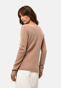 Beżowy sweter z dzianiny z długimi rękawami, okrągłym dekoltem i ściągaczami u rękawów. Miękka tekstura i prosty design, charakteryzujący się czystym, gładkim wykończeniem.