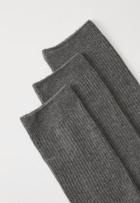 Drei Paar gerippte Socken in Dunkelgrau, mit weicher Textur und sauberen Kanten, übereinander auf einem hellen Hintergrund angeordnet.