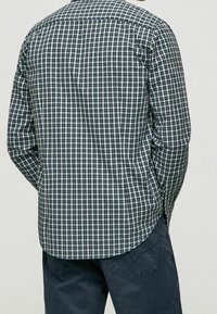 Camicia a quadri verde e blu navy con colletto button-down, maniche lunghe e orlo curvo. Realizzata in un tessuto leggero con una superficie liscia.