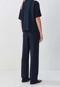 Ensemble deux pièces navy comprenant un haut ample à manches courtes et un pantalon large. Tissu lisse avec un design minimaliste et des lignes épurées.