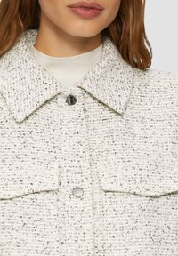 Weiße und graue strukturierte, gewebte Jacke mit einem Kragen, Knopfverschluss und zwei Brusttaschen. Weiche, grobe Stoffdetails.