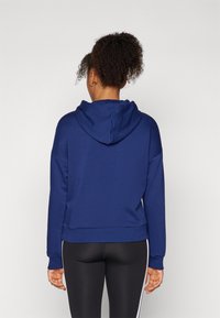 Sweatshirt azul marinho com capuz, apresentando um corte descontraído, mangas longas e um cós canelado. Usado com leggings pretas ajustadas.
