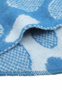 Tessuto di lana blu accogliente con pois bianchi e motivi a scacchi, che mostra una texture morbida e cuciture visibili lungo i bordi.