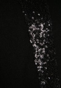 Tissu noir avec un panneau vertical de sequins noirs et argentés densément disposés, créant un contraste de texture et un intérêt visuel.