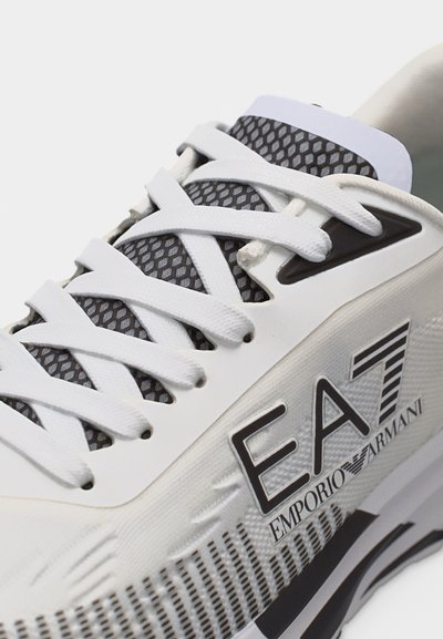 Бяла маратонка Emporio Armani EA7 с бели дантели, черен геометричен дишащ език и брандирана странична панел.