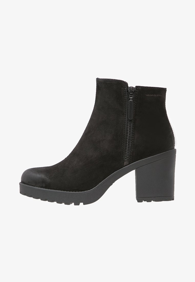 Bottine noire en daim, présentant un design à coupe basse, une fermeture éclair latérale et un talon épais noir avec une semelle extérieure texturée.