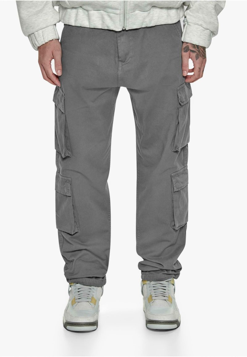 Graue Cargo-Hosen mit mehreren Seitentaschen, einer lockeren Passform und umgeschlagenen Säumen, kombiniert mit grauen und weißen Sneakern.