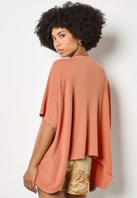 Poncho de punto texturizado color durazno con mangas anchas, corte holgado y escote redondeado, combinado con pantalones cortos estampados.