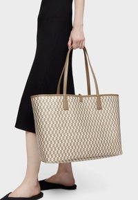 Bolso tote tejido en beige y crema con un patrón geométrico, que cuenta con dos correas de hombro de cuero marrón claro y una textura suave.