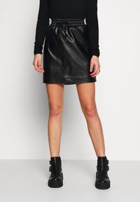 Svart läder mini kjol med elastisk midja och dragsko. Slät textur, rak form och en ren fåll. Matchas med svarta ankelstövlar.