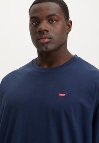 Tricou din bumbac albastru închis, cu mâneci scurte și decolteu rotund. Prezintă un mic logo roșu Levi's pe piept, cu o textură netedă a țesăturii.