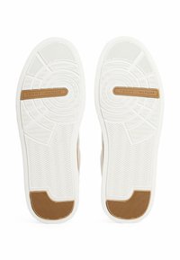 Suole di sneakers bianche con una superficie in gomma testurizzata, che presentano un accento in gomma marrone e il logo "TOMMY HILFIGER" sulla striscia del sottopiede.