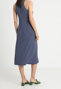 Granatowo-biała, w paski, sukienka midi z plecami w stylu racerback, wyróżniająca się gładką fakturą i nieco rozkloszowanym krojem. W połączeniu z zielonymi sandałami na obcasie.