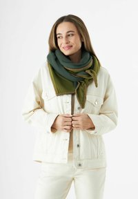 Écharpe verte et olive avec une texture douce, présentant un design noué et des coutures contrastantes marron. Portée sur une veste de couleur claire.