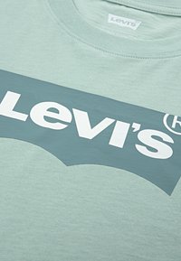 Lys grønn Levi  ’s t-skjorte med en mørkegrønn rektangulær logo og hvit Levi’s-tekst på brystområdet.