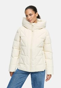 Blouson rembourré crème avec col montant, matelassage diagonal et fermeture éclair sur le devant. Comprend des poches latérales et une finition lisse et texturée.
