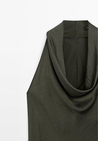 Olivgrön ärmlös topp med draperad cowl-halsringning, som har ett mjukt, strukturerat tyg och en rå kant.