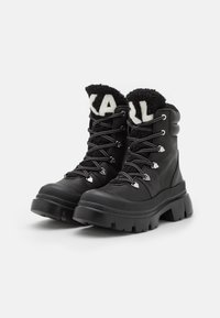 Botas negras con cordones que presentan una parte superior de cuero texturizado, cuello de vellón negro esponjoso con logotipo blanco y suela gruesa de goma.