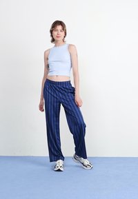 Top court bleu clair associé à un pantalon ample à rayures navy. Le mannequin porte des baskets blanches et se tient contre un fond neutre.