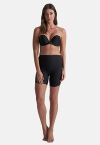 Zwarte strapless beha en hoge taille fietsbroek van gladde stof. Beide stukken zijn aansluitend en naadloos, zonder zichtbare hardware.