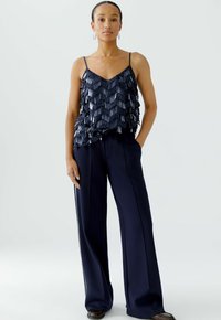 Marineblaues ärmelloses Top mit geschichteten Fransen Details, kombiniert mit weit geschnittenen marineblauen Hosen. Beide Kleidungsstücke verfügen über eine elegante, glatte Textur.