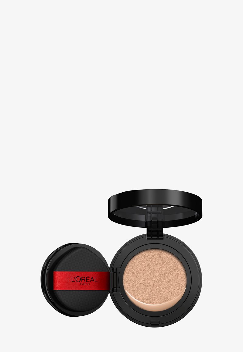 Compact foundation in een ronde, zwarte doos met een rood accent. Heeft een beige kussen aan de binnenkant, dat een gladde, gestructureerde oppervlakte toont.