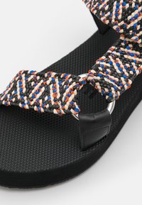 Czarna sandał na kostkę z plecionym, wielokolorowym wierzchem z tkaniny, z wzorami w kolorze pomarańczowym, niebieskim i kremowym; detal ze srebrnym wykończeniem.